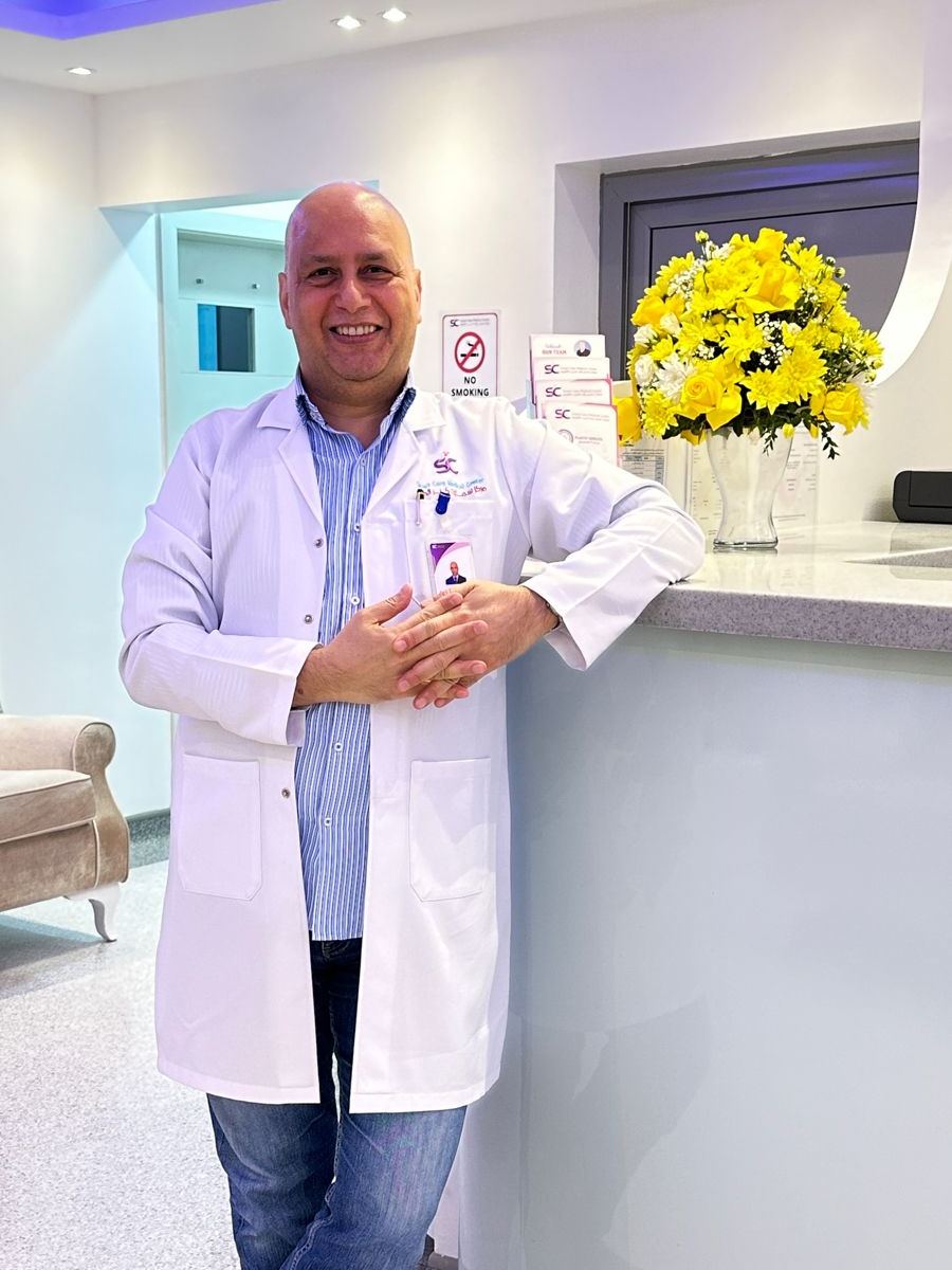 Dr. Hussein in a white coat, leaning on the reception desk at his clinic